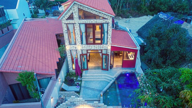 A two-story house with a swimming pool, stone exterior, and a red roof. - La Rocca An Bang beach (Da Nang)
