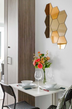 A dining area with a white table, black chairs, a vase with flowers, and a hexagonal mirror on the wall. - Cozy Studio Near Southern Cross with City Views (Melbourne)