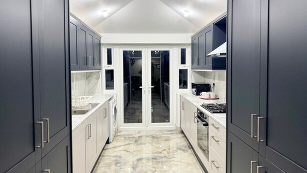 A modern kitchen with dark cabinets, white countertops, and a marble floor. - Modern North London Retreat - 7 Bedrooms (London)