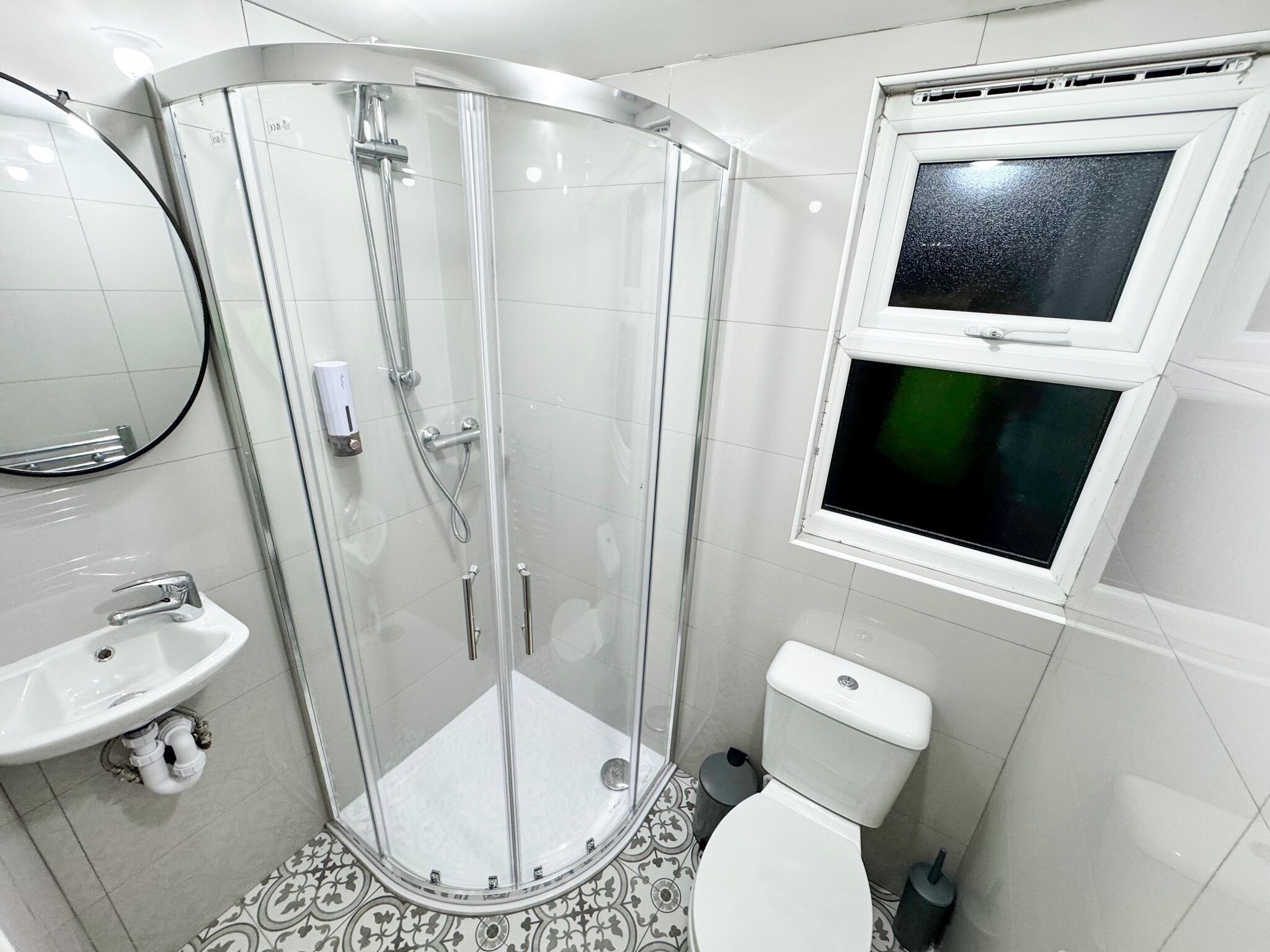 Un baño con ducha envuelta en vidrio, inodoro, lavamanos y ventana con vistas al exterior.