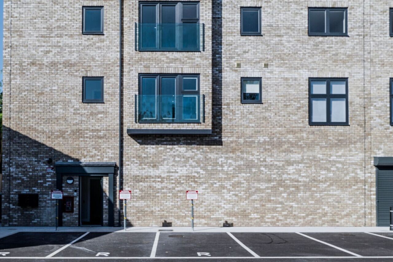A multi-story building with a brick facade, multiple windows, and a parking lot with marked spaces.