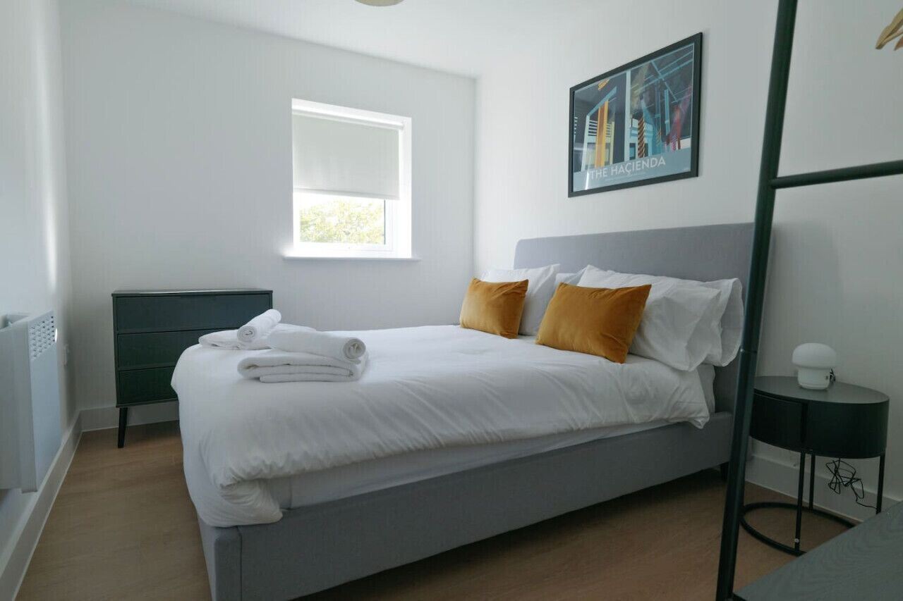 Un dormitorio moderno con una cama, una ventana, un cuadro y una mesita de noche.