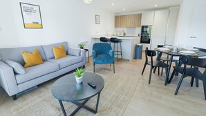 A modern living room with a sofa, coffee table, and chairs, a kitchen with a dining area, and a small island.