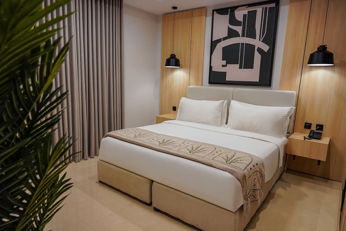 A modern bedroom with a large bed, bedside tables, and a wall-mounted artwork.
