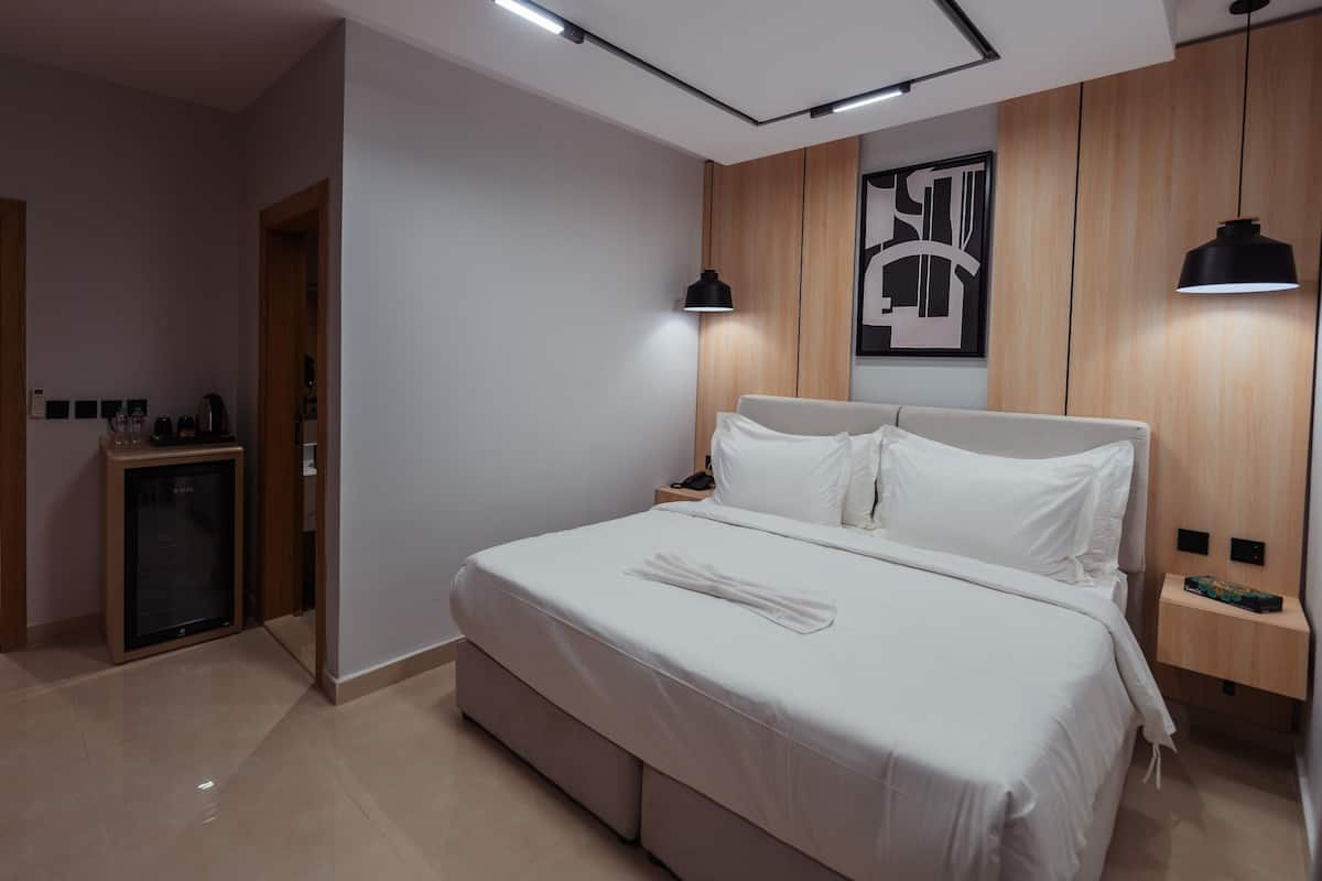 A modern bedroom with a large bed, a bedside table, a nightstand, a wall-mounted artwork, and a ceiling light fixture.