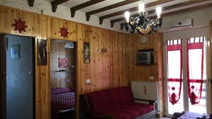 Ein gemütliches Zimmer mit Holzwänden, einem Bett, einer Couch, einem Fernseher und einem Fenster mit Vorhängen.