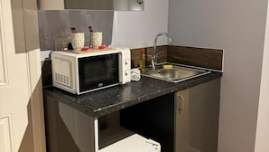 Een kleine keuken met een magnetron, spoelbak en twee decoratieve vazen op het aanrecht.