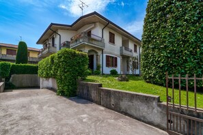 A two-story house with a balcony, a concrete driveway, and a well-maintained garden.