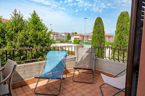 A balcony with two chairs, one with a blue cover and one with a white cover, and a concrete wall.