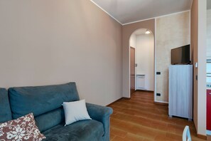 A living room with a sofa, a television, and a kitchen area in the background.