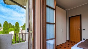 Un balcon donnant sur des arbres et des immeubles, une porte en bois et un lit avec un oreiller marron.