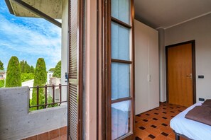 A balcony with a view of trees and buildings, a wooden door, and a bed with a brown pillow.