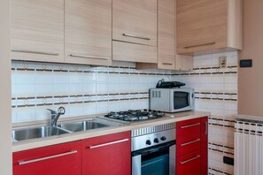 A kitchen with a gas stove, microwave, sink, and red cabinets.