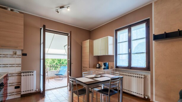 Une cuisine compacte avec un coin repas, une porte-fenêtre coulissante donnant sur une terrasse extérieure et une vue sur la verdure.