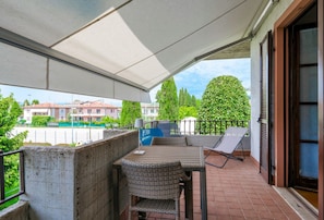 A balcony with a table and chairs, a chair with a sunshade, and a view of buildings and greenery.