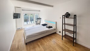 A bedroom with a bed, a TV mounted on the wall, a window with a view of trees, and a shelf with a vase. - Magnificent 158m² loft in Caluire le bas, 10mm from Lyon 6,  (Caluire-et-Cuire)