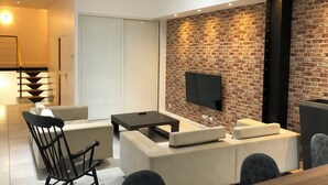 A modern living room with a brick wall, a flat-screen TV, and a sofa. - Magnificent 158m² loft in Caluire le bas, 10mm from Lyon 6,  (Caluire-et-Cuire)