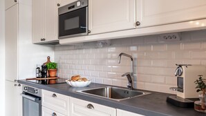 Una cuina moderna amb armaris blancs, forn integrat, rentapesos d'acer inoxidable i cafetera.