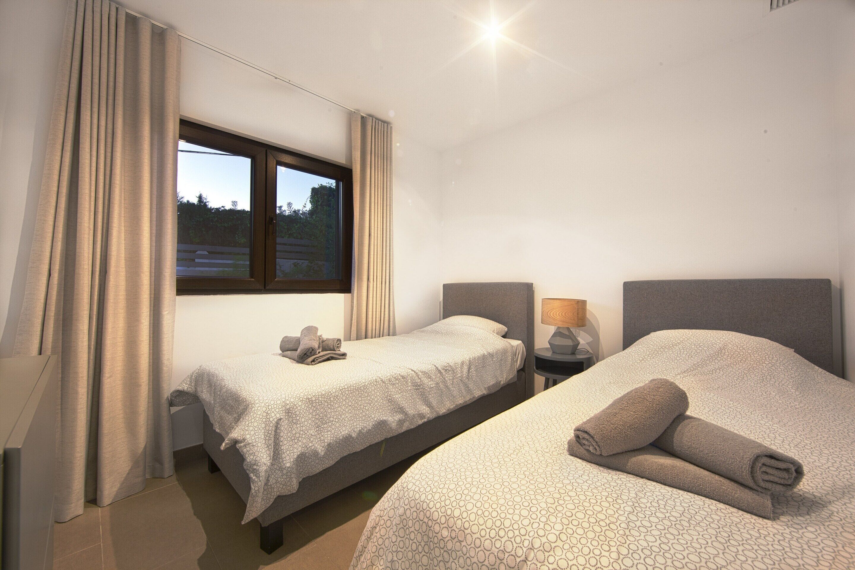A hotel room with two beds, a window with curtains, and a nightstand with a lamp.
