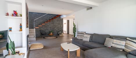 Una sala de estar moderna con un sofá gris, una mesa de centro blanca y una escalera con pared de piedra.