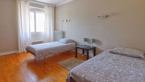 Une chambre avec deux lits, une petite table avec des lampes, un radiateur et une fenêtre avec des rideaux.