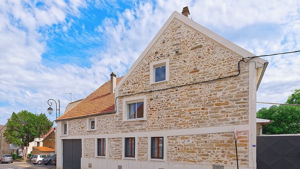 Un bâtiment en pierre doté d’un toit à forte pente, de nombreuses fenêtres et d’une entrée fermée par un portail.