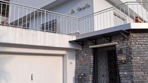 A modern two-story building with a white facade, a stone entrance, and a balcony with metal railings.