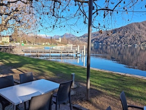 A lakeside dining area with a table and chairs, a dock, and a view of a mountain and buildings in the background.
