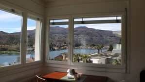 A room with a view of a lake and mountains. There is a table with a chair and a small statue on it.