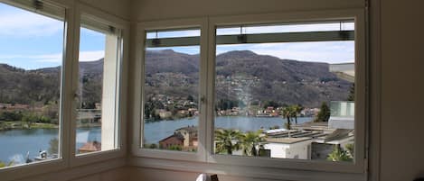 A room with a view of a lake and mountains. There is a table with a chair and a small statue on it.