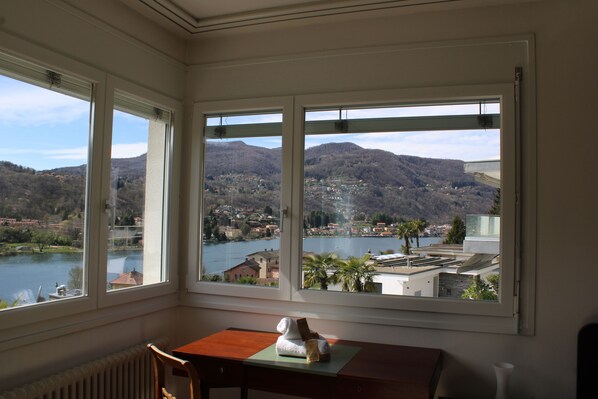 A room with a view of a lake and mountains. There is a table with a chair and a small statue on it.