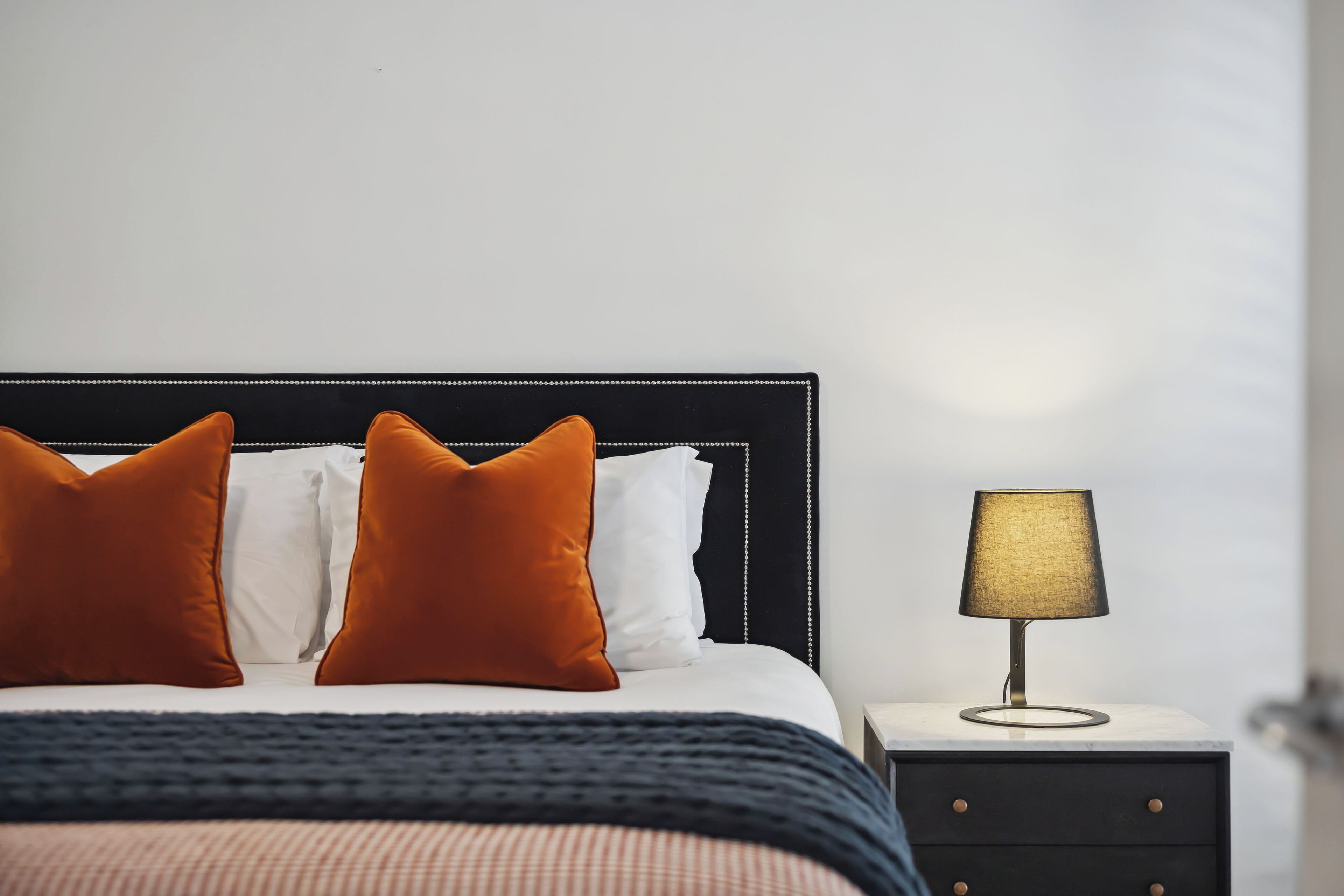 Una cama bien hecha con dos almohadas naranjas, una blanca y una manta azul oscuro.