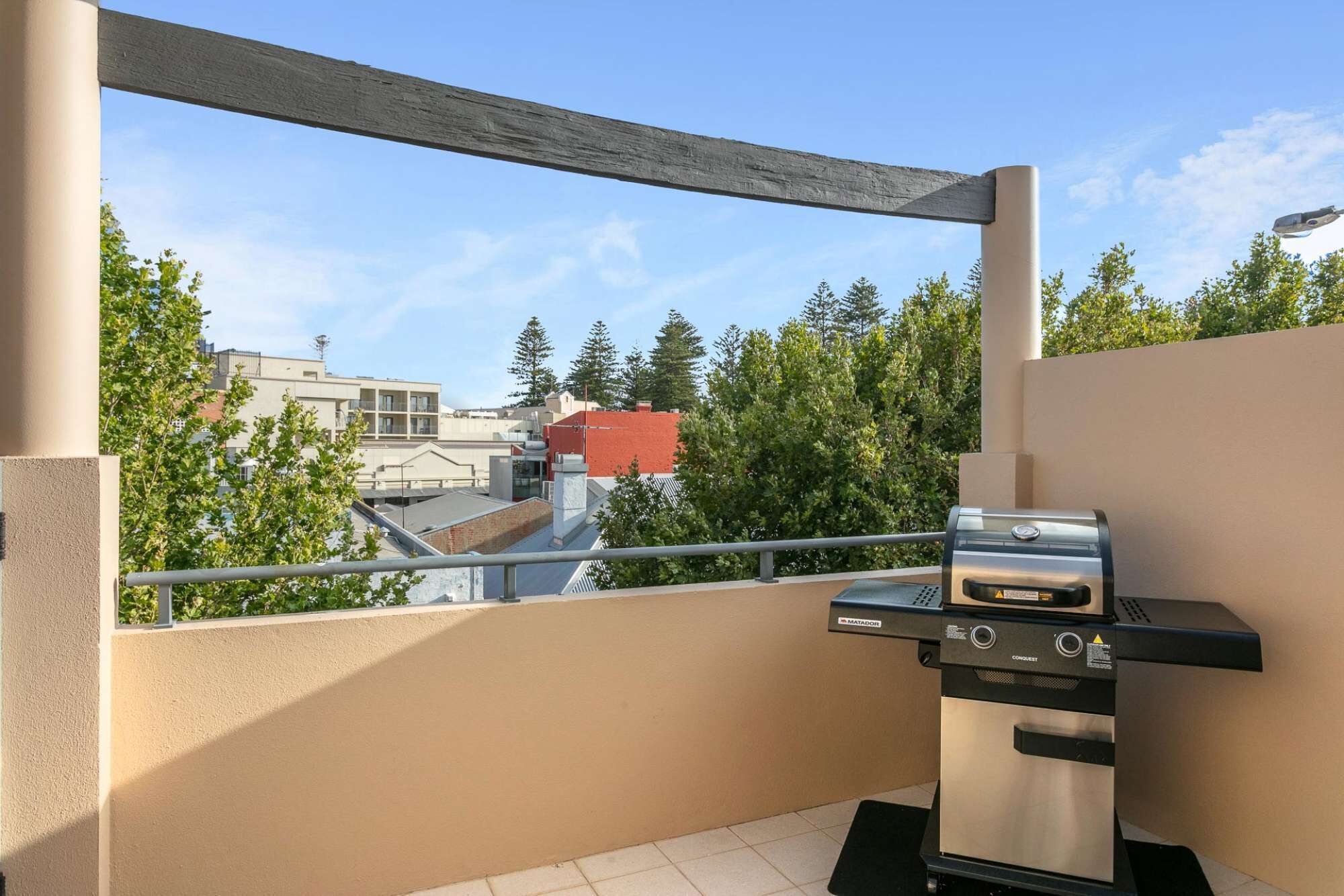 Un balcon avec un barbecue, une vue sur les immeubles et les arbres.