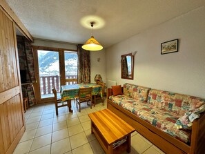 A cozy living room with a wooden sofa, a wooden bench, a dining table with chairs, and a view of a snowy mountain through large windows. - Charming Termignon apartment for 4, 27m² with Wifi (Termignon)