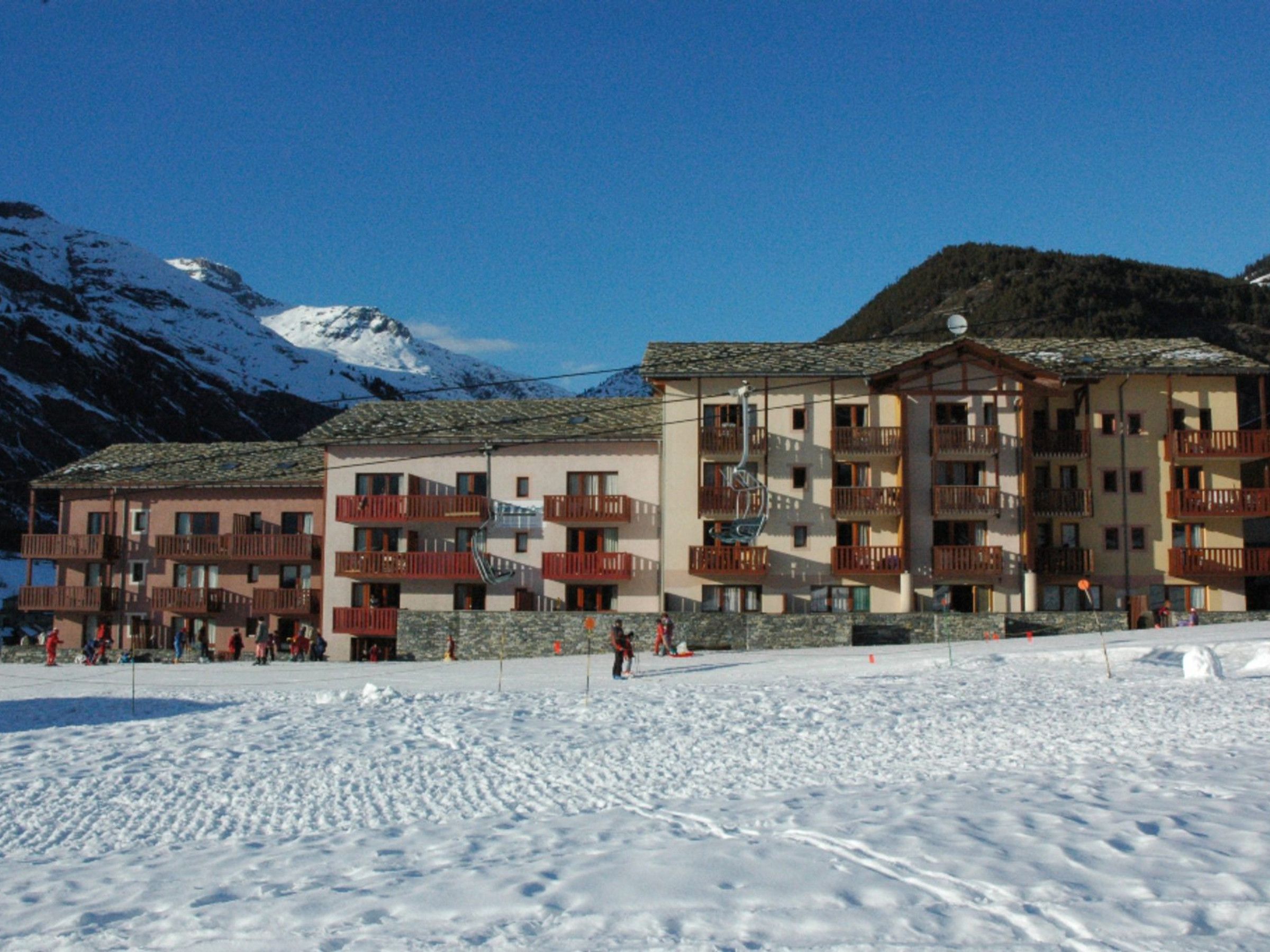 A multi-story hotel with balconies and a ski slope in the background.