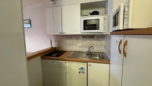 A compact kitchen with white cabinets, a built-in microwave, a sink, and a dishwasher.