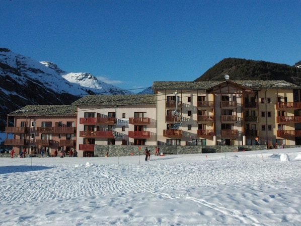 A multi-story hotel with balconies and a ski slope in the background.