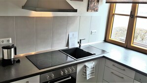 A modern kitchen with a black induction cooktop, a stainless steel coffee maker, and a window with a view of the outdoors. - Modern Strata Montana vacation apartment with garden, underfloor heating and air conditioning (Bensheim)
