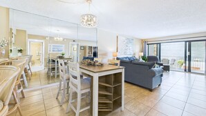 A spacious living area with a dining table, chairs, a sofa, and a balcony with a view. - Sandcastles 2BR/2BA Cocoa Beach Ocean Views! Heated Pool! (Cocoa Beach)