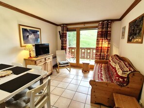 Una habitación con televisión, una mesa de comedor, un sofá y un balcón con cortinas estampadas.