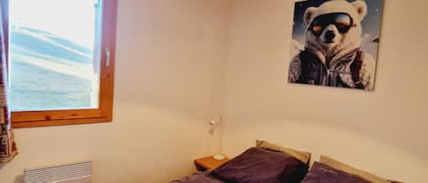 A bedroom with a bed, a window, a wall-mounted lamp, and a poster of a bear.