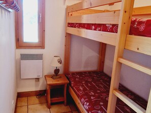 Ein kleiner, gemütlicher Raum mit einem Etagenbett, einem Heizgerät, einem Fenster und einem Nachttisch mit Lampe.