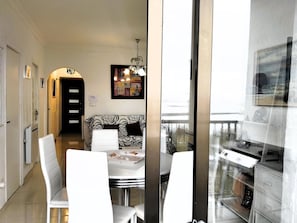 A dining area with a white table and chairs, a black and white patterned sofa, and a chandelier.