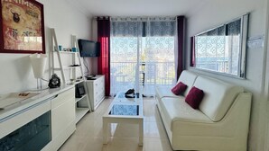 A living room with a white sofa, a coffee table, a TV, and a balcony with a view.