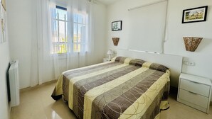 A bedroom with a bed, a window with curtains, a bedside table, a lamp, and two wall-mounted baskets.