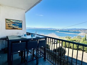 Uma varanda com uma mesa posta para refeições, com vista para a costa, barcos e um porto de iates.