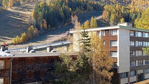 A modern building with a stone facade and a wooden structure in the foreground. A ski lift is visible in the background, surrounded by autumn-colored trees. - Renovated studio for 4, south, near slopes and mall (Pra-Loup)