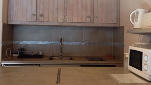A kitchen with wooden cabinets, a tiled backsplash, a stainless steel sink, a microwave, and pendant lights. - Renovated studio for 4, south, near slopes and mall (Pra-Loup)