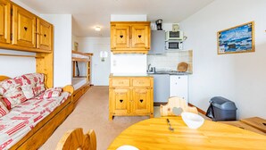 A compact room with a bunk bed, wooden cabinets, a small kitchenette, and a dining area.