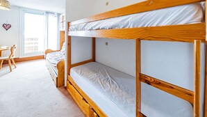 A bunk bed room with a wooden frame, a desk with chairs, and a window with curtains.
